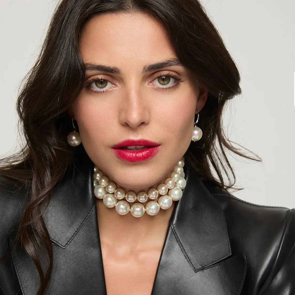 Nahaufnahme eines Models mit Perlenohrringen und zweireihigem Choker, neutraler Hintergrund.