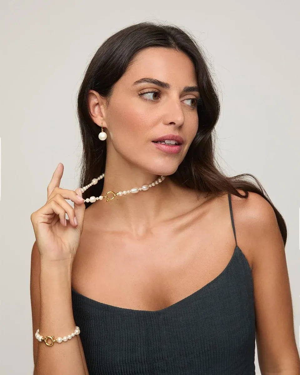 Model mit Perlenhalskette und Creolen, Dreiviertelansicht vor neutralem Hintergrund.