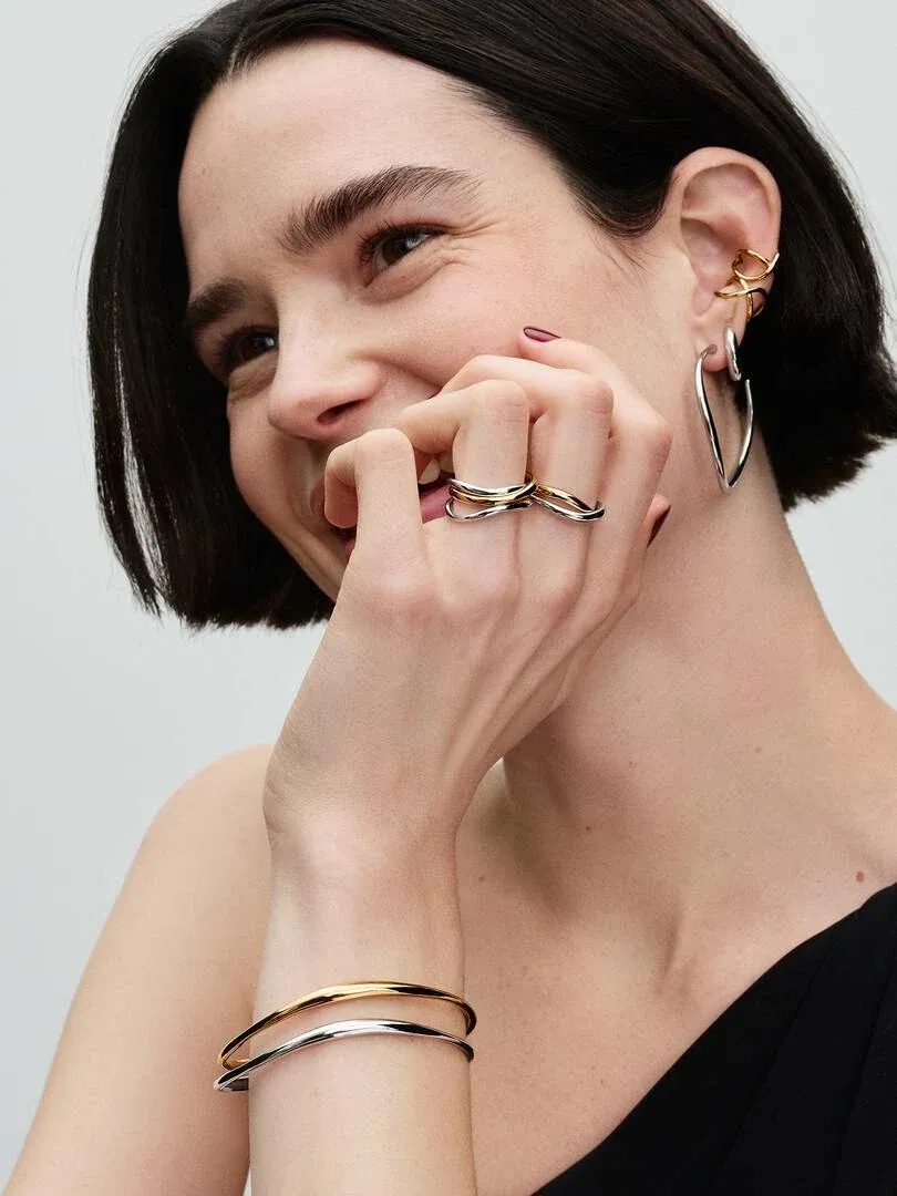 Close-up van lachend model met tweekleurige verstrengde ring en armband, neutrale achtergrond.