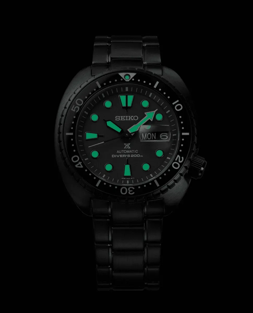 Full front view of a black watch on a solid black background, highlighting the green luminescent indices.