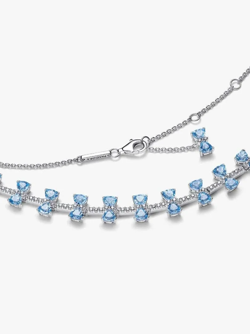 Close-up van de zilveren ketting met blauwe kristallen strikjes op een witte achtergrond, diagonale hoek.