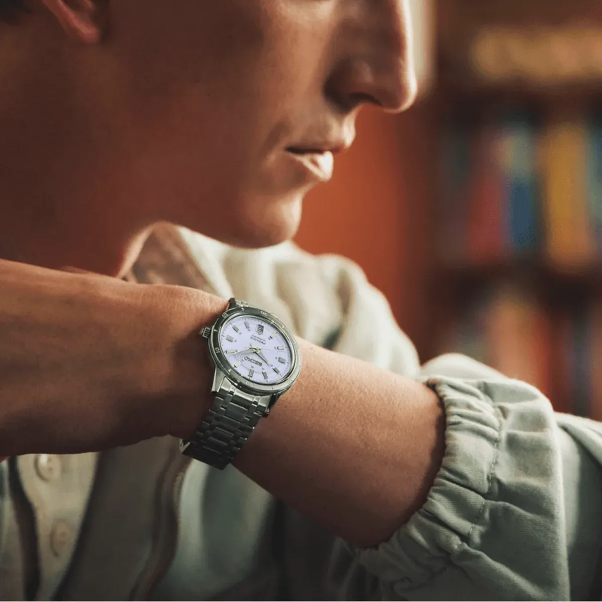 Watch on a man's wrist, profile shot with a blurred warm interior background.