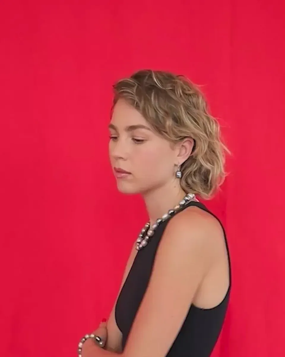 Modelo de perfil con collar y pulsera de perlas barrocas, fondo rojo sólido, plano medio.