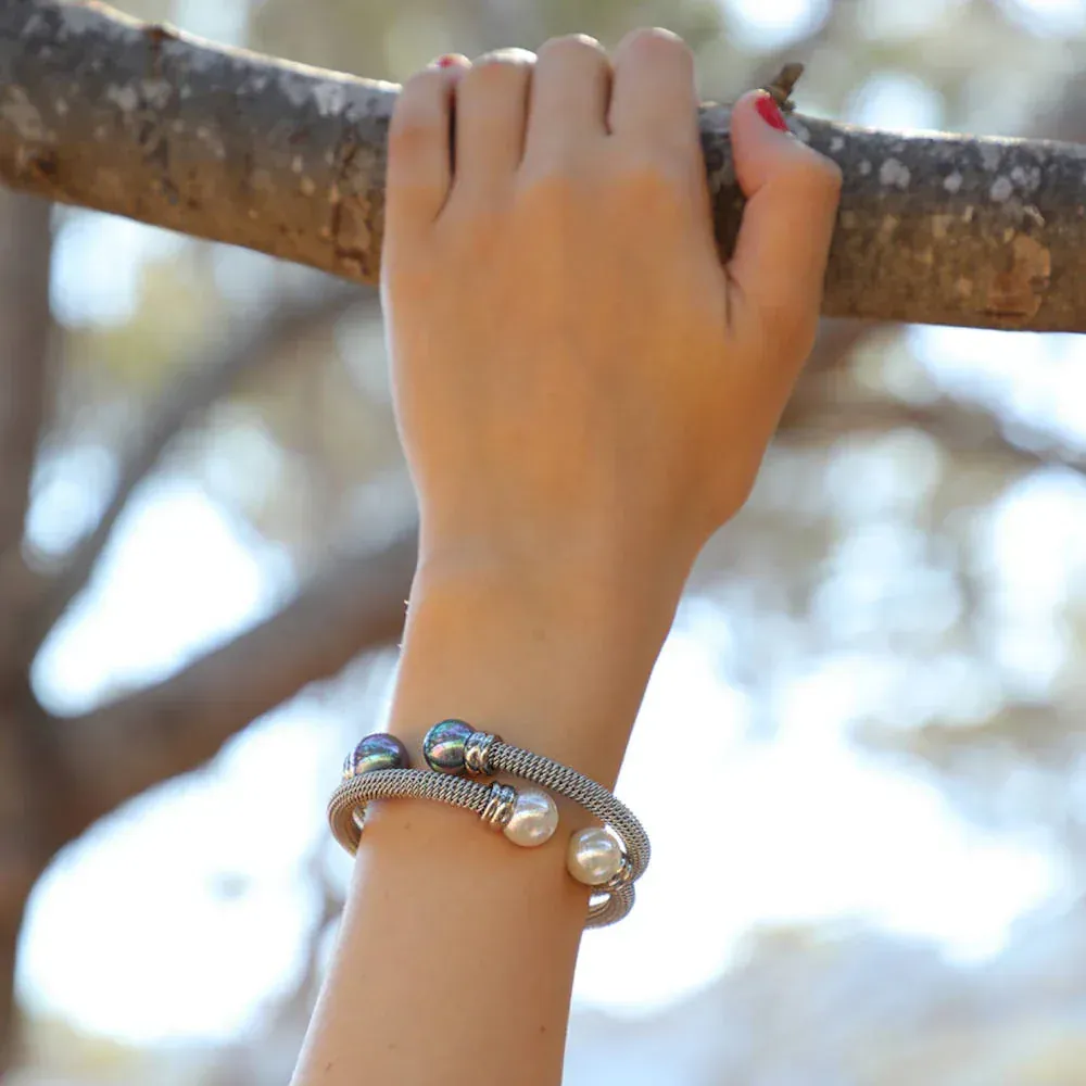 Brazaletes de perlas puestos en muñeca, mano sujetando rama de árbol, fondo natural desenfocado