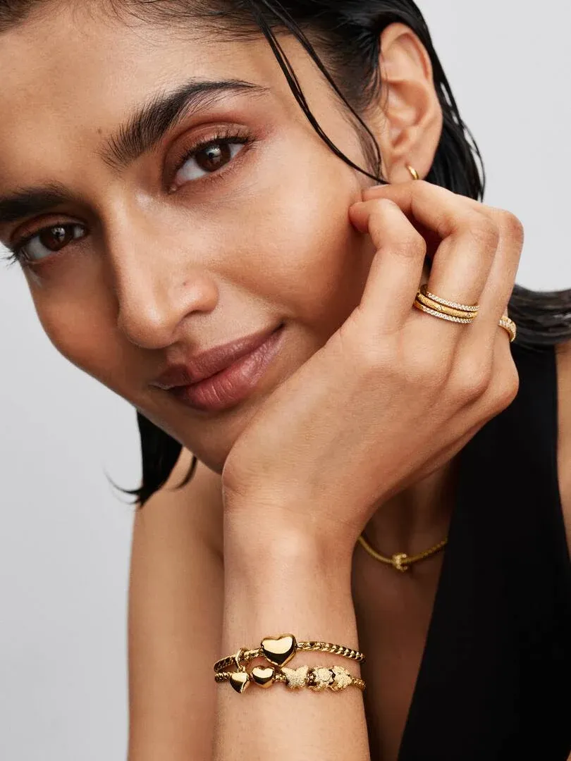 Nahaufnahme des Handgelenks mit goldenen Armbändern und Ringen, Modell stützt Gesicht auf die Hand.
