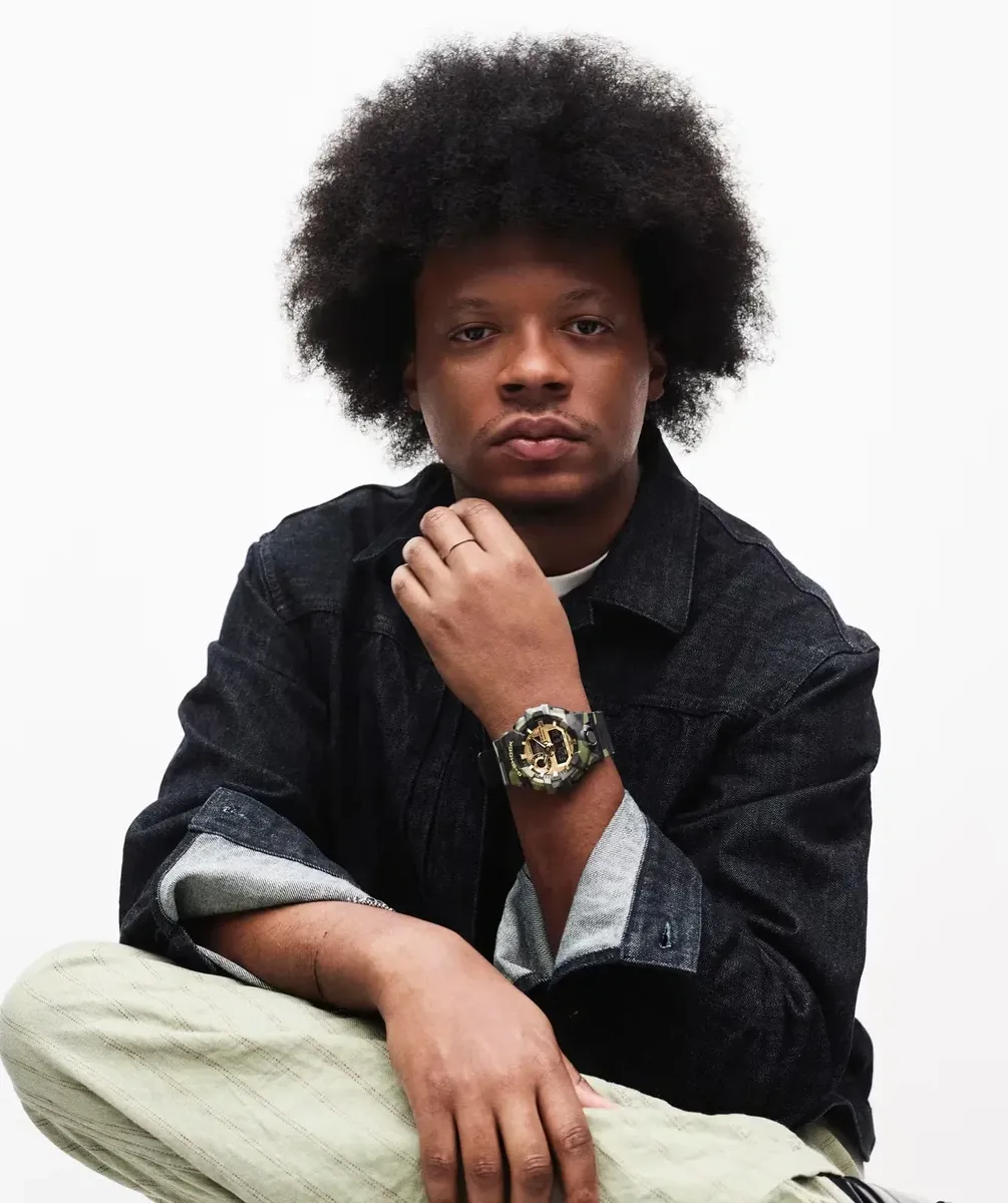 Plano medio de modelo masculino luciendo el reloj en la muñeca, fondo blanco, vestimenta estilo urbano.