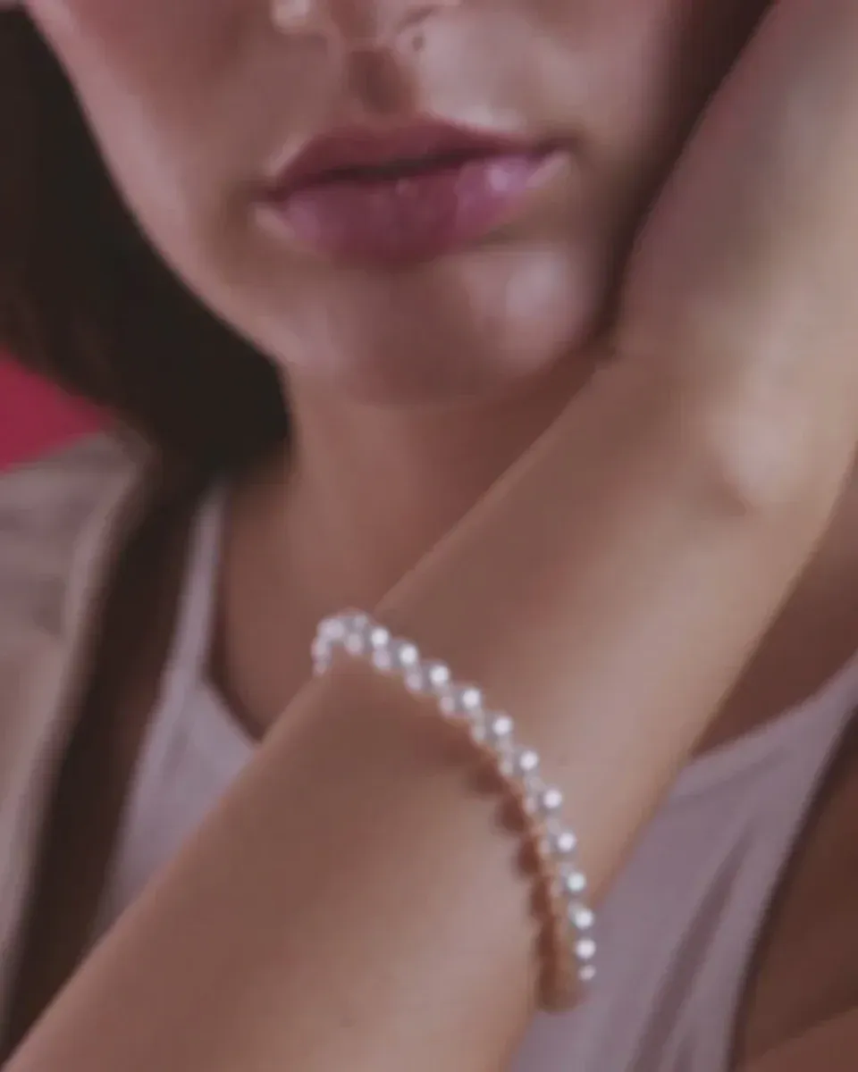Primer plano de la pulsera de perlas en la muñeca, toma lateral con modelo y fondo desenfocado.