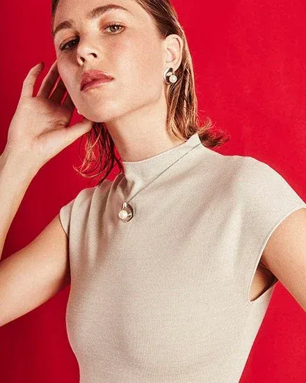Modelo con cuello alto vistiendo el collar de perla y pendientes a juego, fondo rojo vibrante.