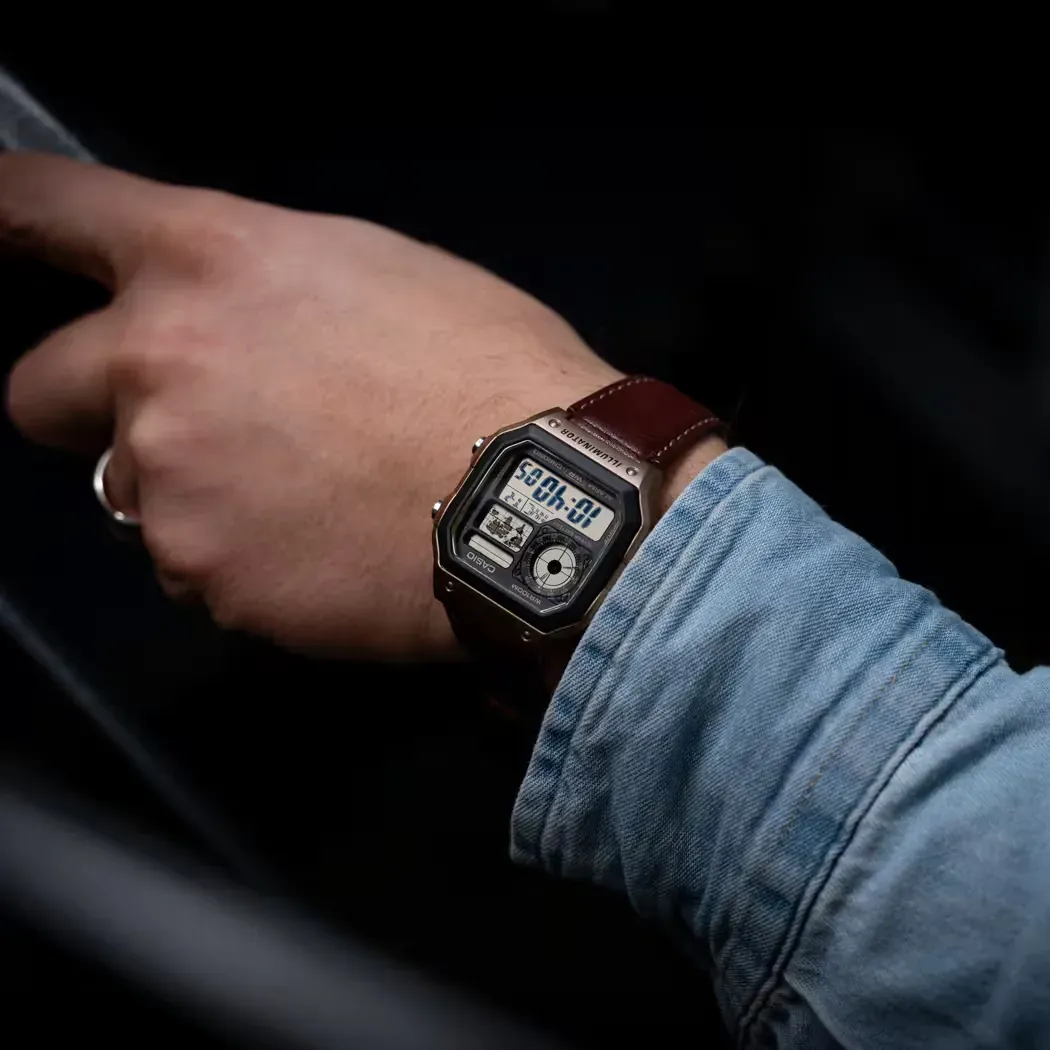 Reloj puesto en la muñeca de un modelo con camisa vaquera, fondo oscuro desenfocado.