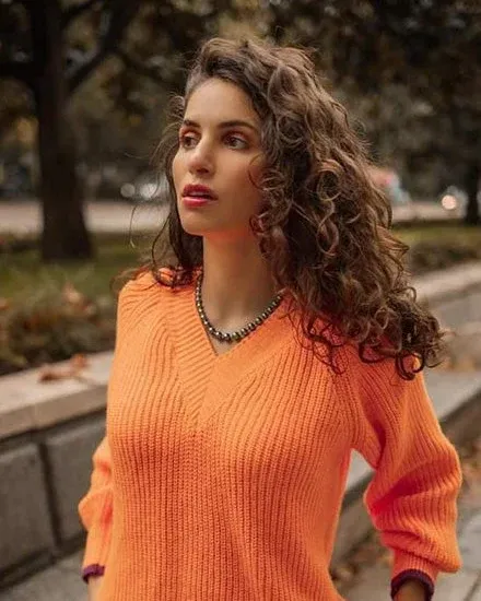 Collar de perlas sobre cuello de modelo con jersey naranja, toma media en exterior con fondo desenfocado.