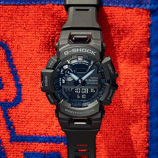 Vista frontal del reloj colocado sobre una superficie de tela texturizada en colores rojo y azul.