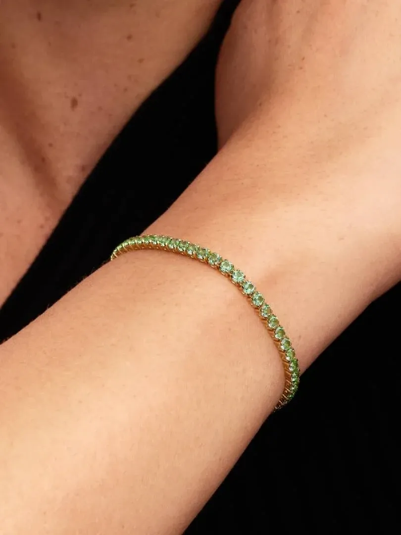 Close-up van de tennisarmband met groene kristallen om een pols, zijaanzicht tegen een zwarte achtergrond.