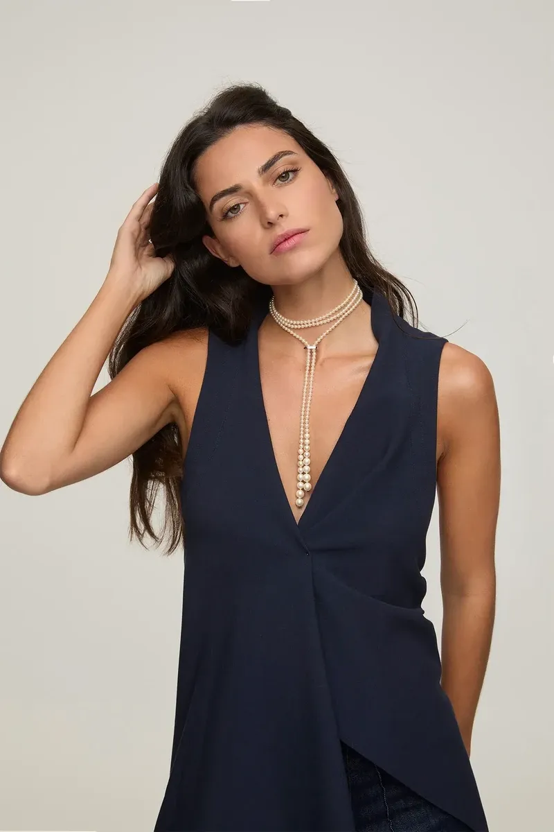 Mannequin avec collier de perles en double tour et chute verticale, plan moyen de profil, fond neutre.