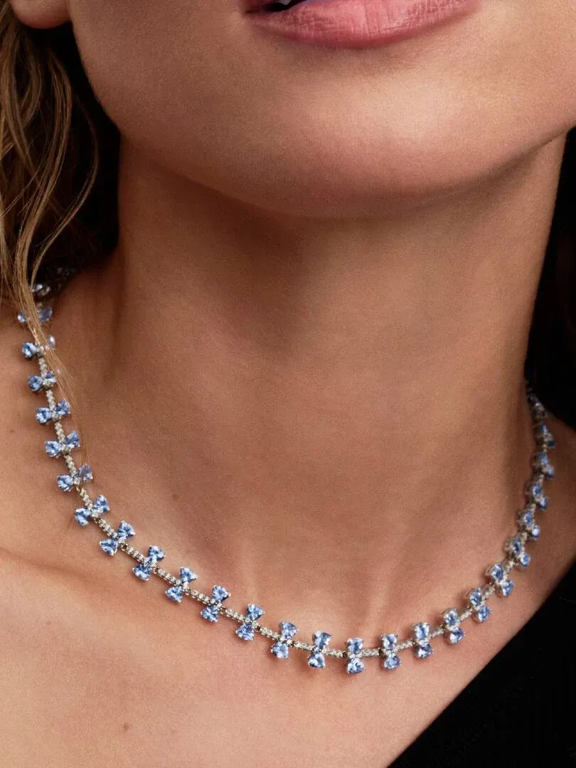 Close-up van de blauwe strikketketting om de hals van een model, frontaal shot met focus op de kristallen.