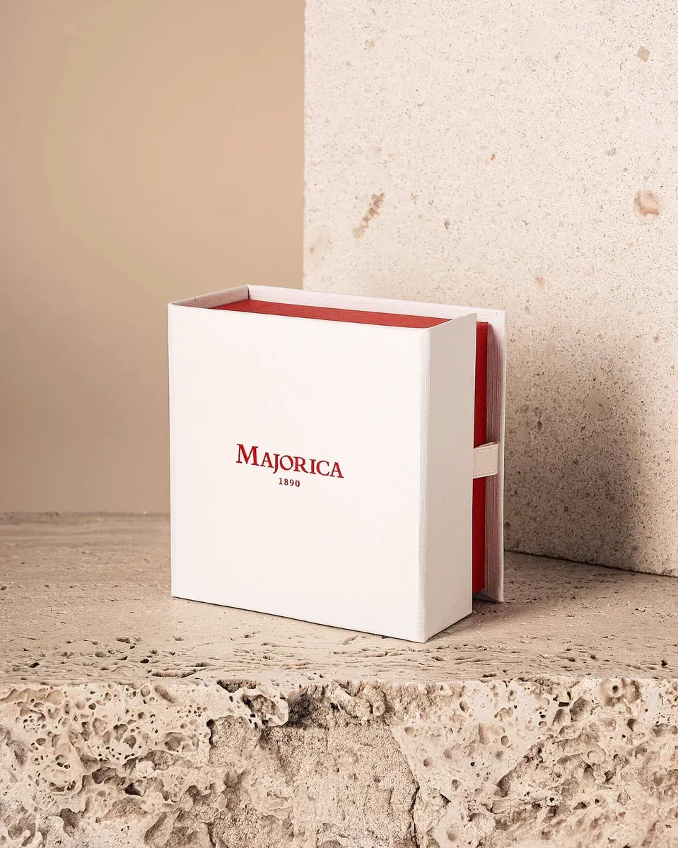Weiße Majorica-Schachtel mit rotem Logo, schräg auf einer natürlichen Steinoberfläche präsentiert.
