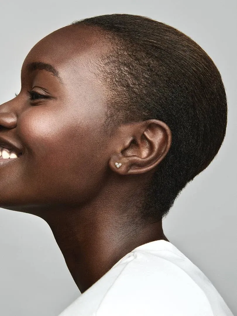 Profile close-up of a model wearing the heart-shaped stud earring, neutral gray background.