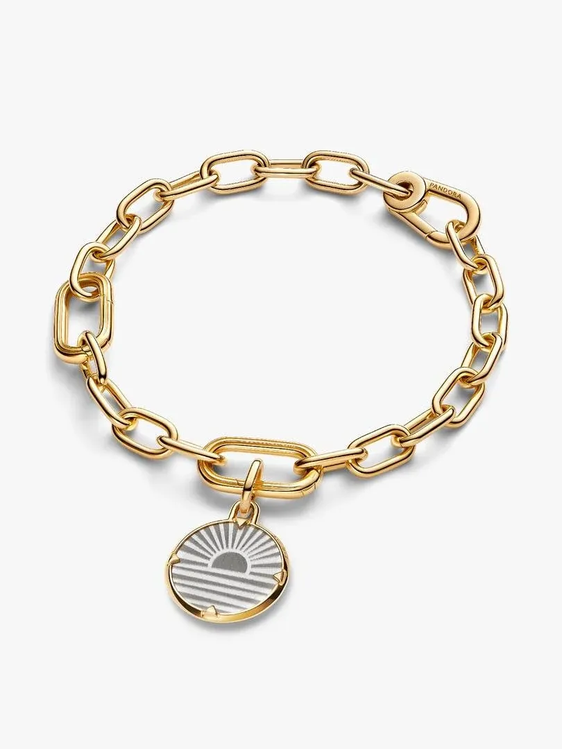 Charm médaillon lever de soleil sur un bracelet à maillons dorés, vue plongeante sur fond blanc.