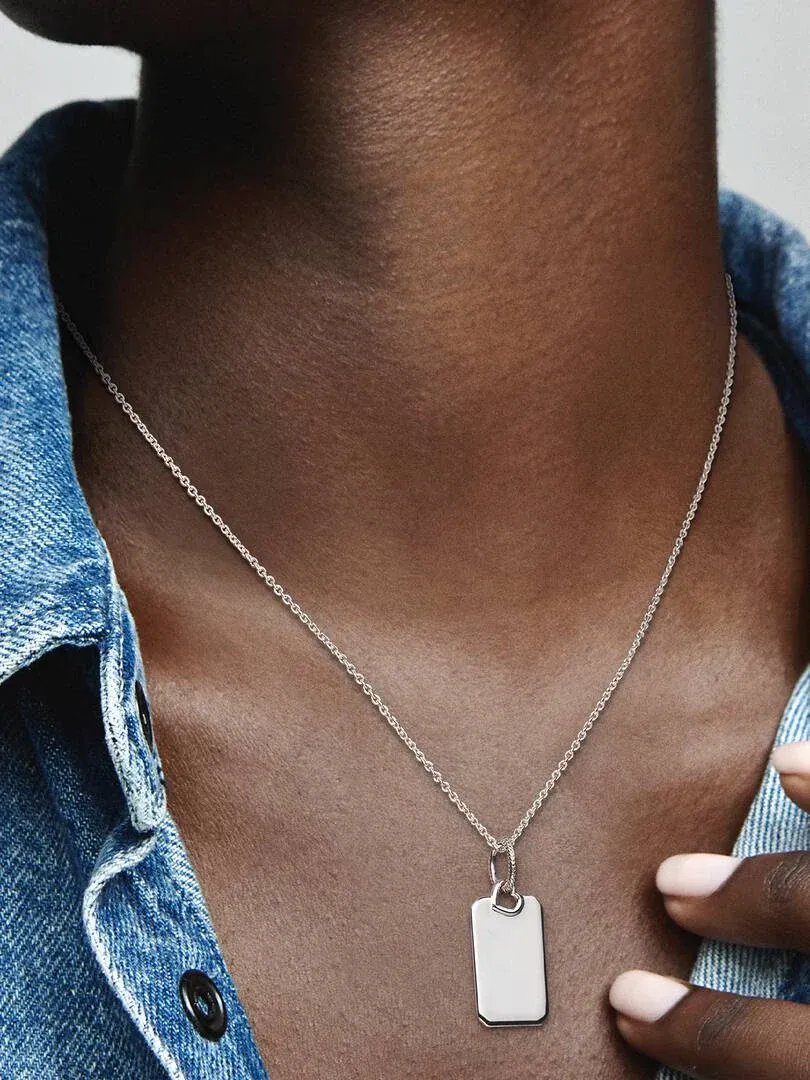 Primer plano del colgante rectangular de plata sobre el cuello, con camisa de mezclilla azul.