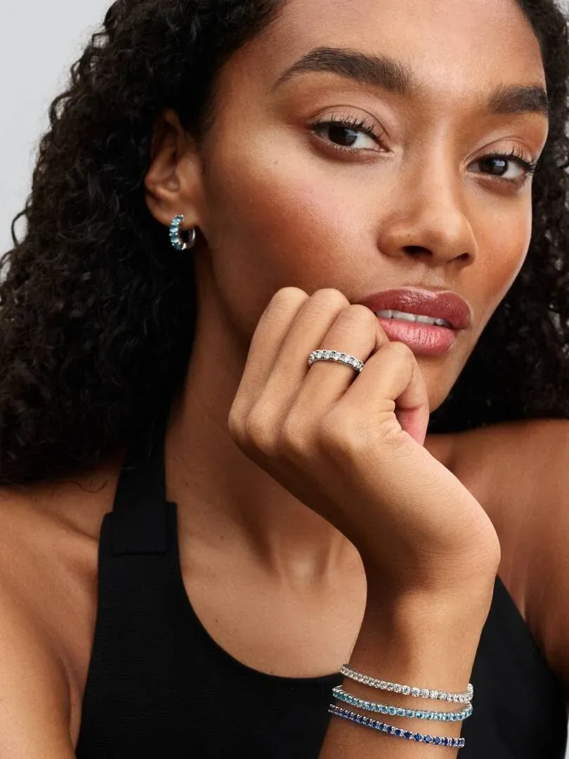 Nahaufnahme eines Models mit blauem Tennisarmband und Creolen, Seitenansicht vor neutralem Hintergrund.