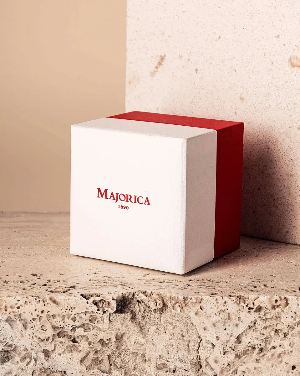 Caja de joyería blanca y roja con logotipo, situada sobre una superficie de piedra texturizada.