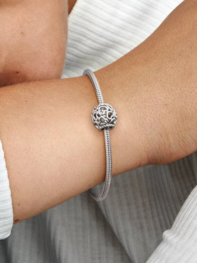 Close-up van een hartvormige charm aan een zilveren armband, gedragen om de pols tegen een witte achtergrond.