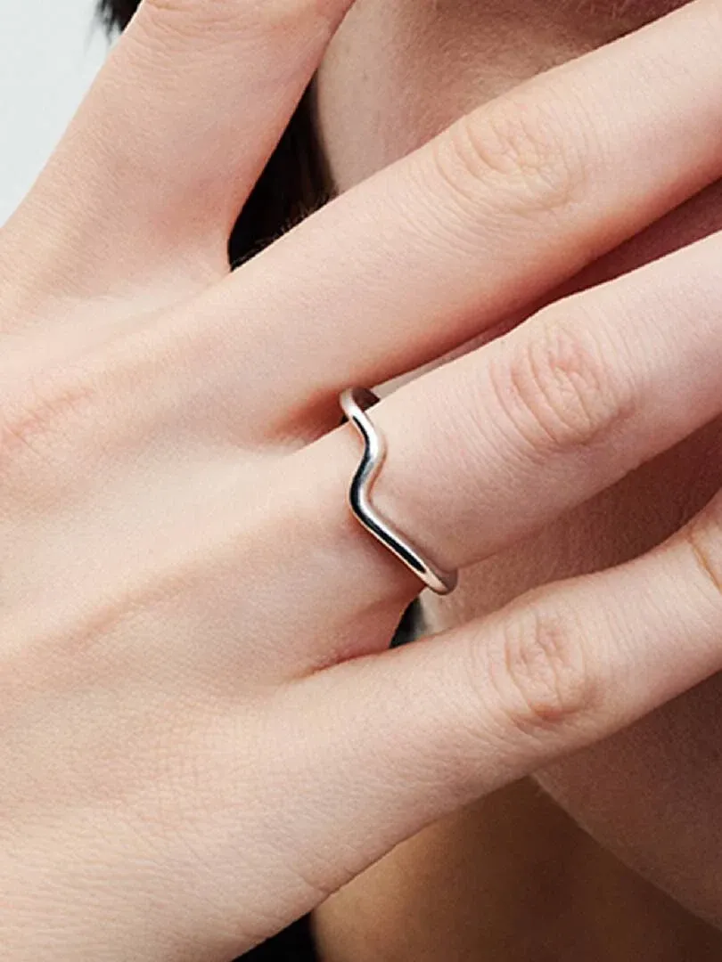 Seitenansicht des wellenförmigen Silberrings am Finger, vor weichem, unscharfem Hauthintergrund.