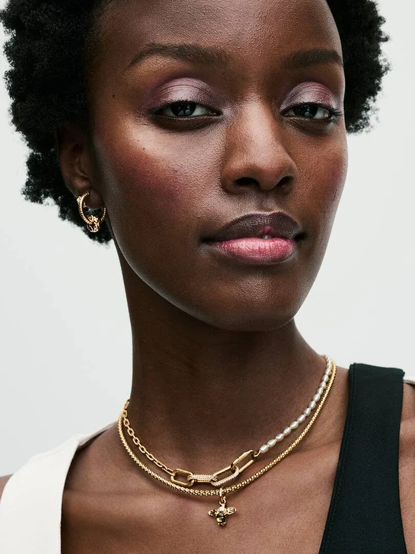 Close-up van model met gouden ketting en bijpassende oorbellen, lichte neutrale achtergrond.