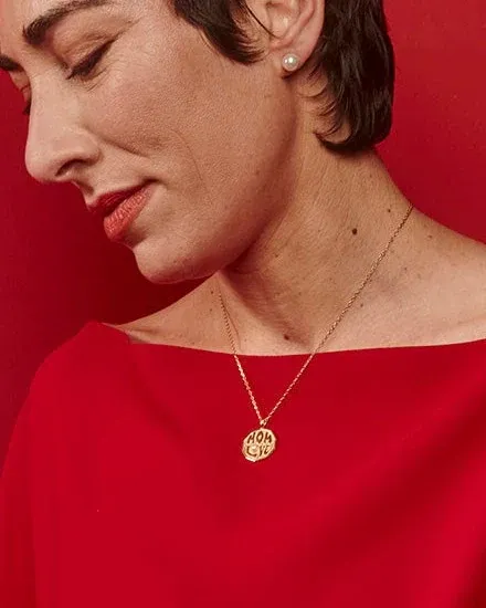 Zijaanzicht close-up van een vrouw met een gouden medaillenhalsketting en pareloorbellen tegen een rode achtergrond.