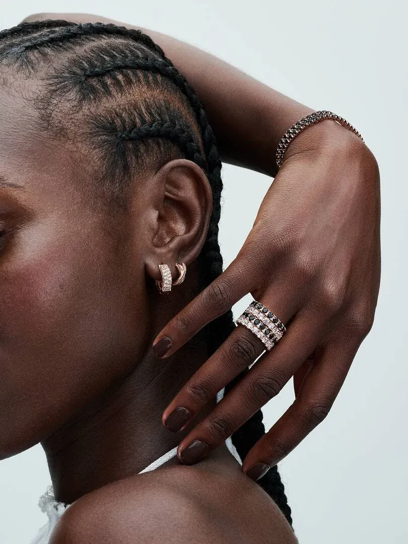 Nahaufnahme einer Hand mit schwarzem Eternity-Ring und passenden Ohrringen, Profil vor weißem Hintergrund.