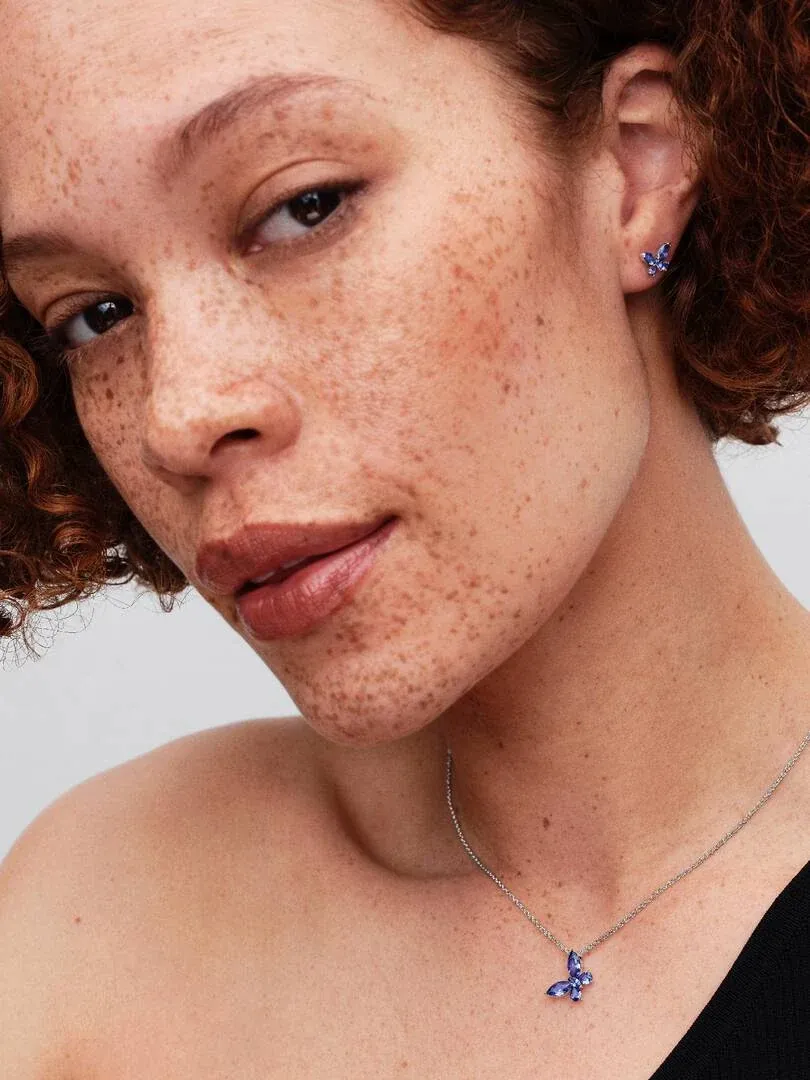 Nahaufnahme eines Models mit der blauen Schmetterlingskette und passenden Ohrringen, Seitenansicht vor neutralem Hinterg