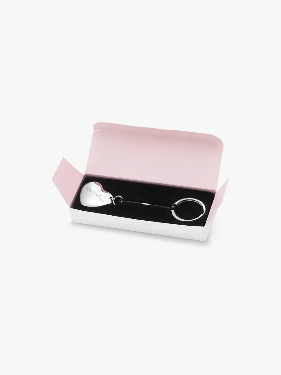 Heart-shaped jewelry opener inside an open pink gift box, viewed from a high angle.