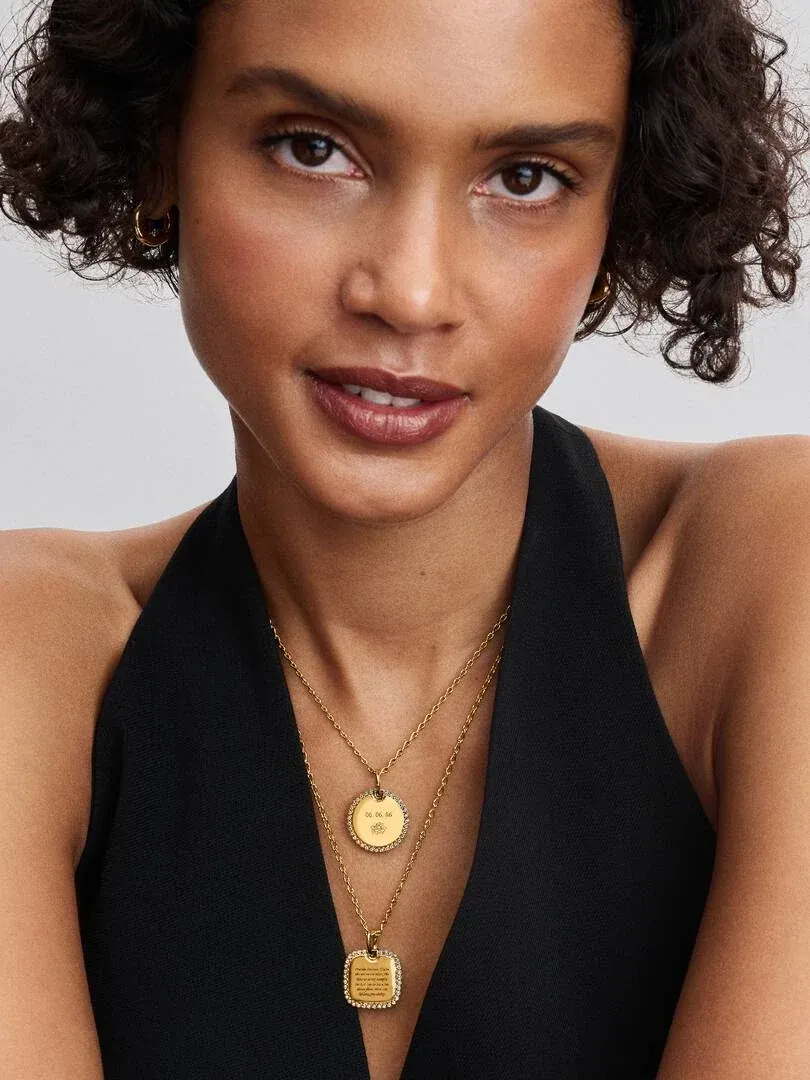 Gros plan de deux pendentifs dorés avec zircons sur le cou d'un mannequin, fond neutre.