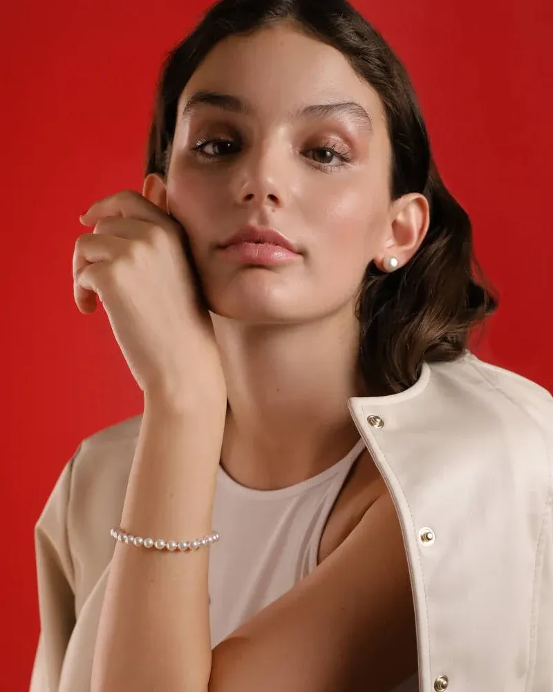 Close-up of pearl bracelet on wrist, model against vibrant red background, front view.