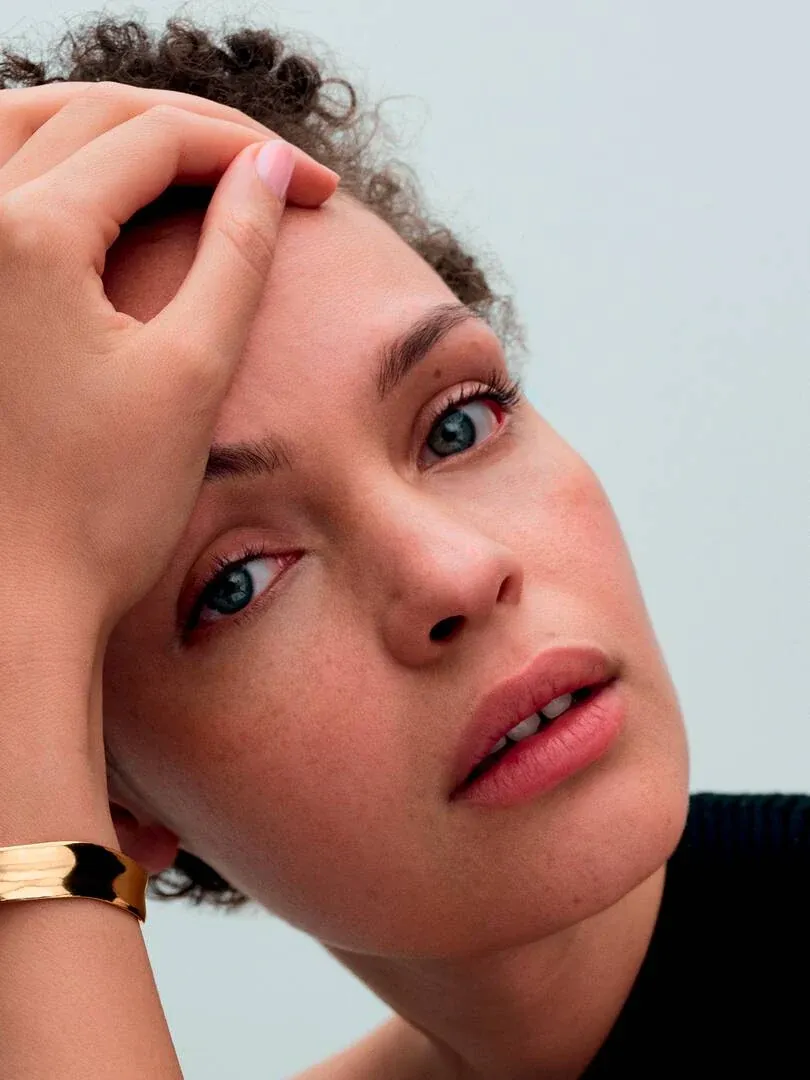 Close-up of model wearing a gold bangle on the wrist, side view against a light neutral background.