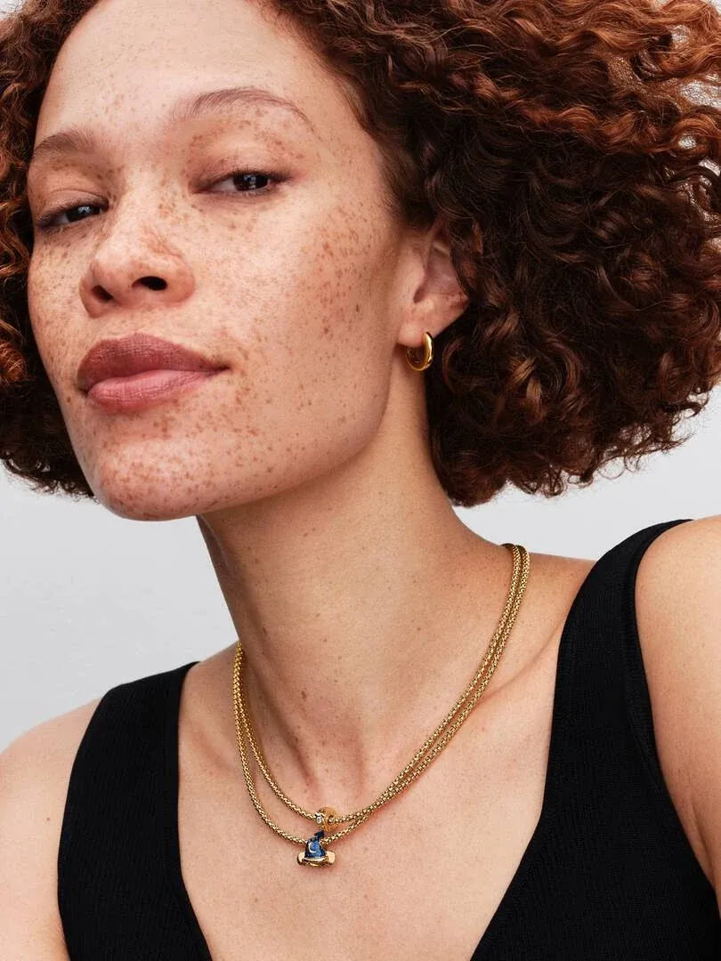 Close-up of a model wearing a double gold chain necklace and hoop earrings against a neutral background.