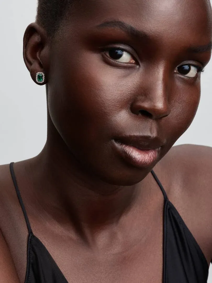 Close-up of rectangular green stud earring on earlobe, front view with neutral background.