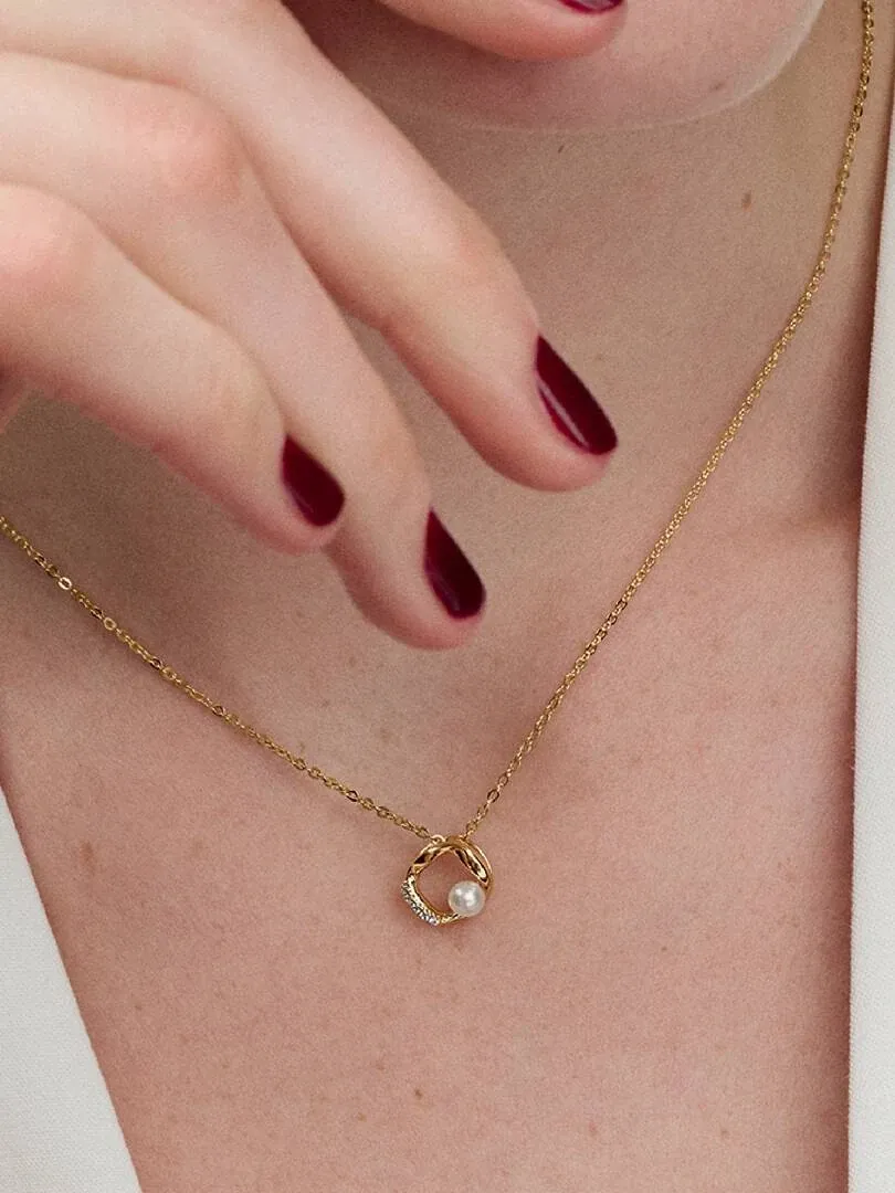 Primer plano del collar con perla y pavé sobre el cuello de una modelo, toma frontal con mano cerca.