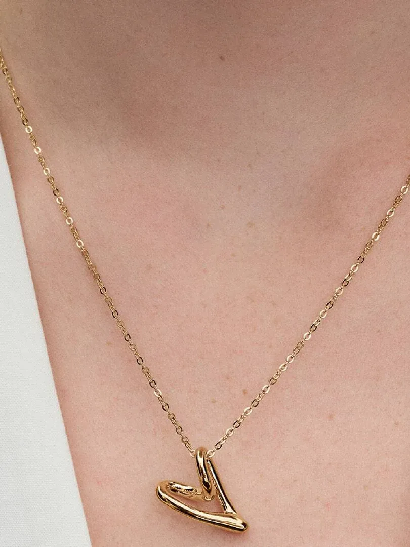 Primer plano de collar con colgante de corazón orgánico sobre el cuello de una modelo, fondo neutro.