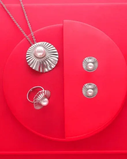 Set aus Halskette, Ring und Ohrringen auf rotem Rundsockel, Draufsicht mit radialen Metalltexturen.