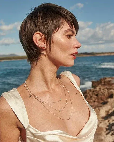 Seitenprofil einer Frau mit einer mehrreihigen Perlenkette, unscharfer Hintergrund mit Meer und Küste.