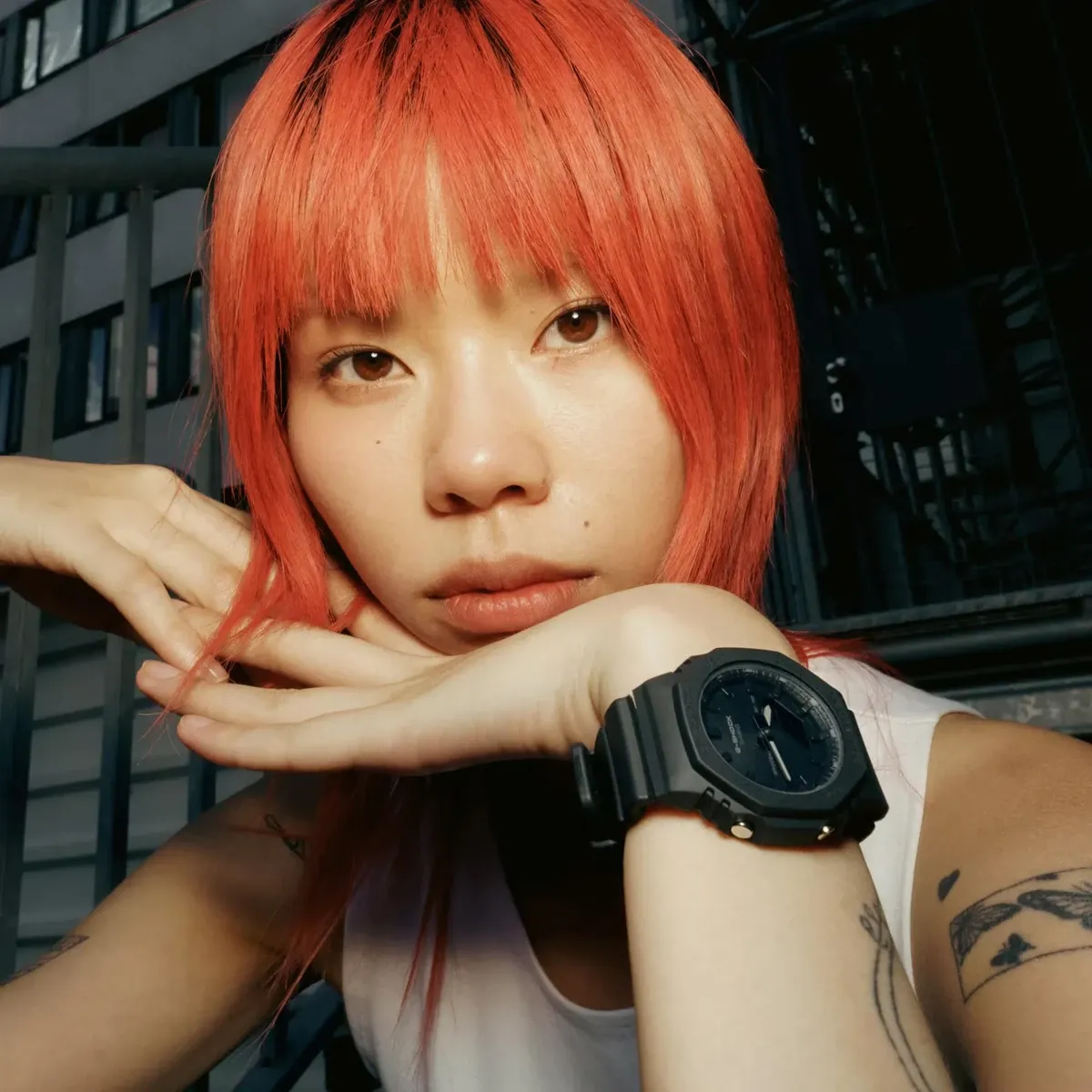 Retrato de modelo con cabello rojo y reloj en la muñeca, fondo urbano industrial.
