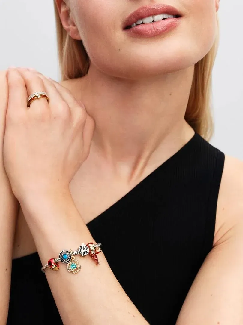 Close-up of a woman wearing a charm bracelet and ring, side view against a neutral background.