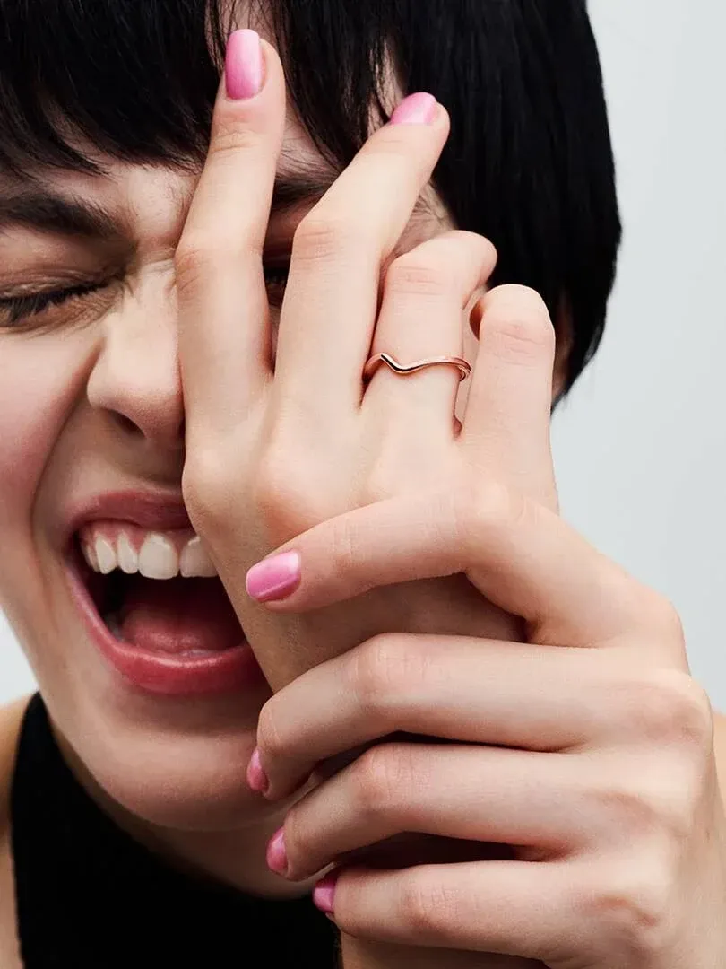 Close-up van handen met roze nagels met de golvende ring, zijaanzicht voor het gezicht van een model.