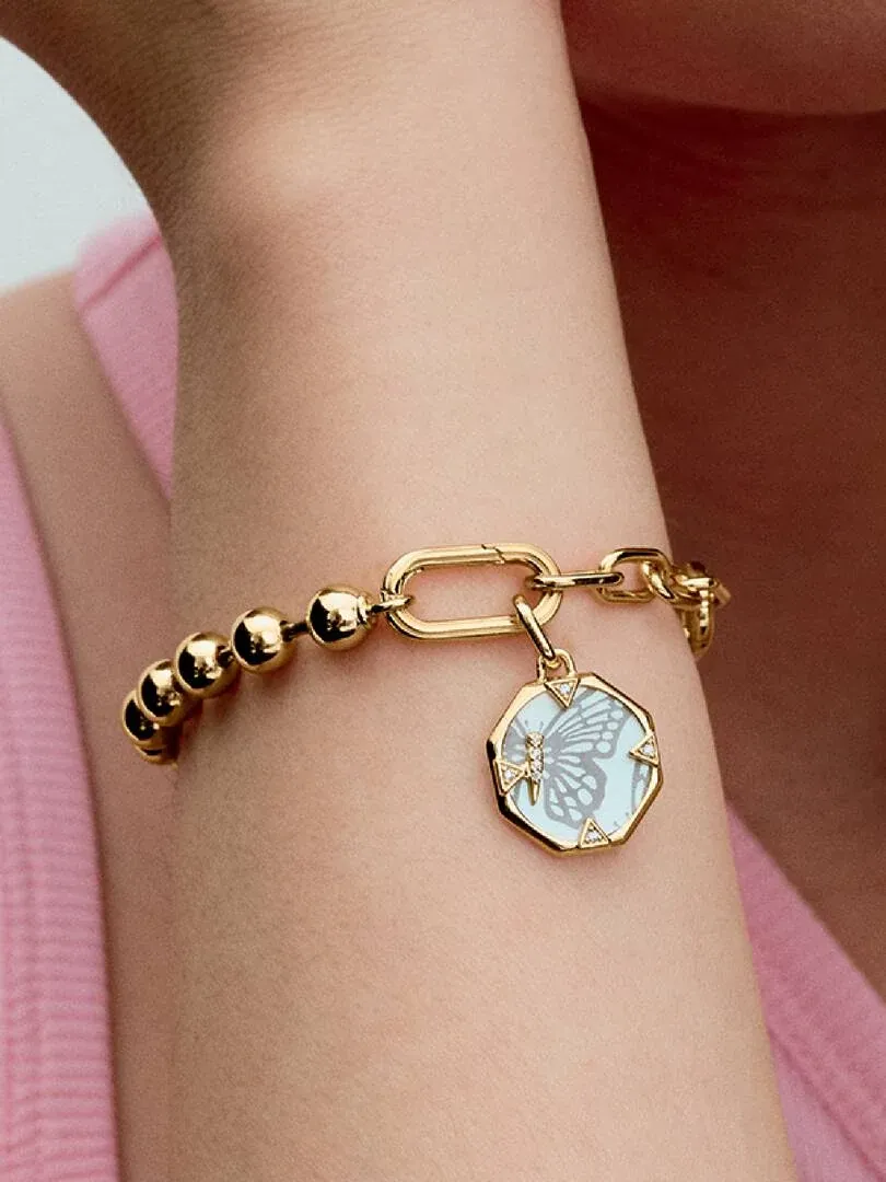 Nahaufnahme des Armbands mit achteckigem Anhänger am Handgelenk, Seitenansicht vor weichem rosa Hintergrund.