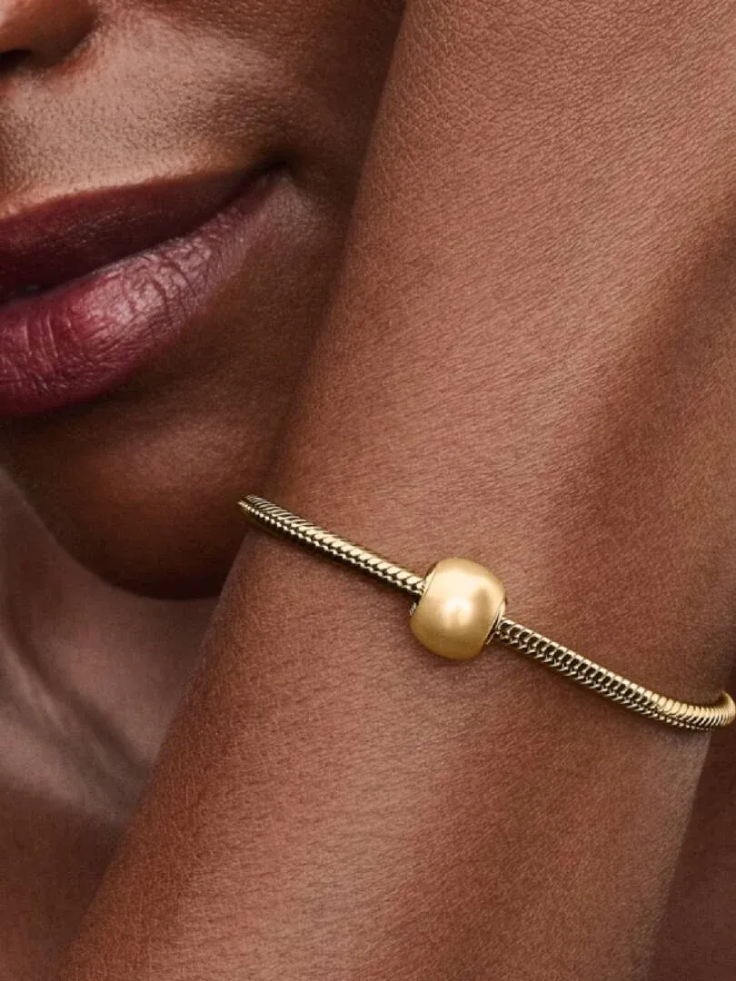 Close-up of a yellow pearl charm on a gold bracelet, worn on a model's wrist.