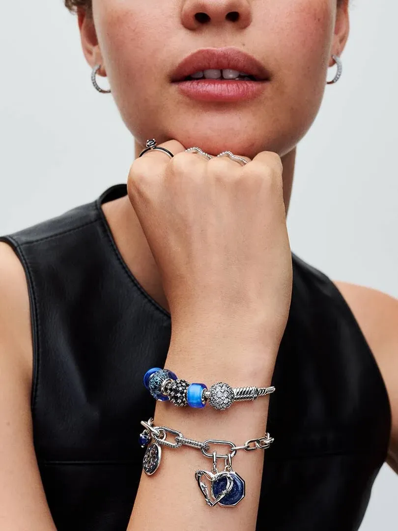 Gros plan d'un bracelet avec charms bleus et bagues sur la main, fond neutre.