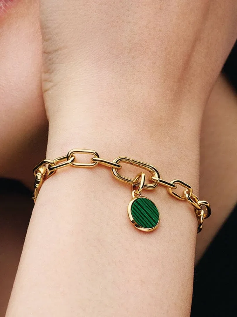 Primer plano de pulsera de eslabones dorados con charm de medallón verde sobre la muñeca.