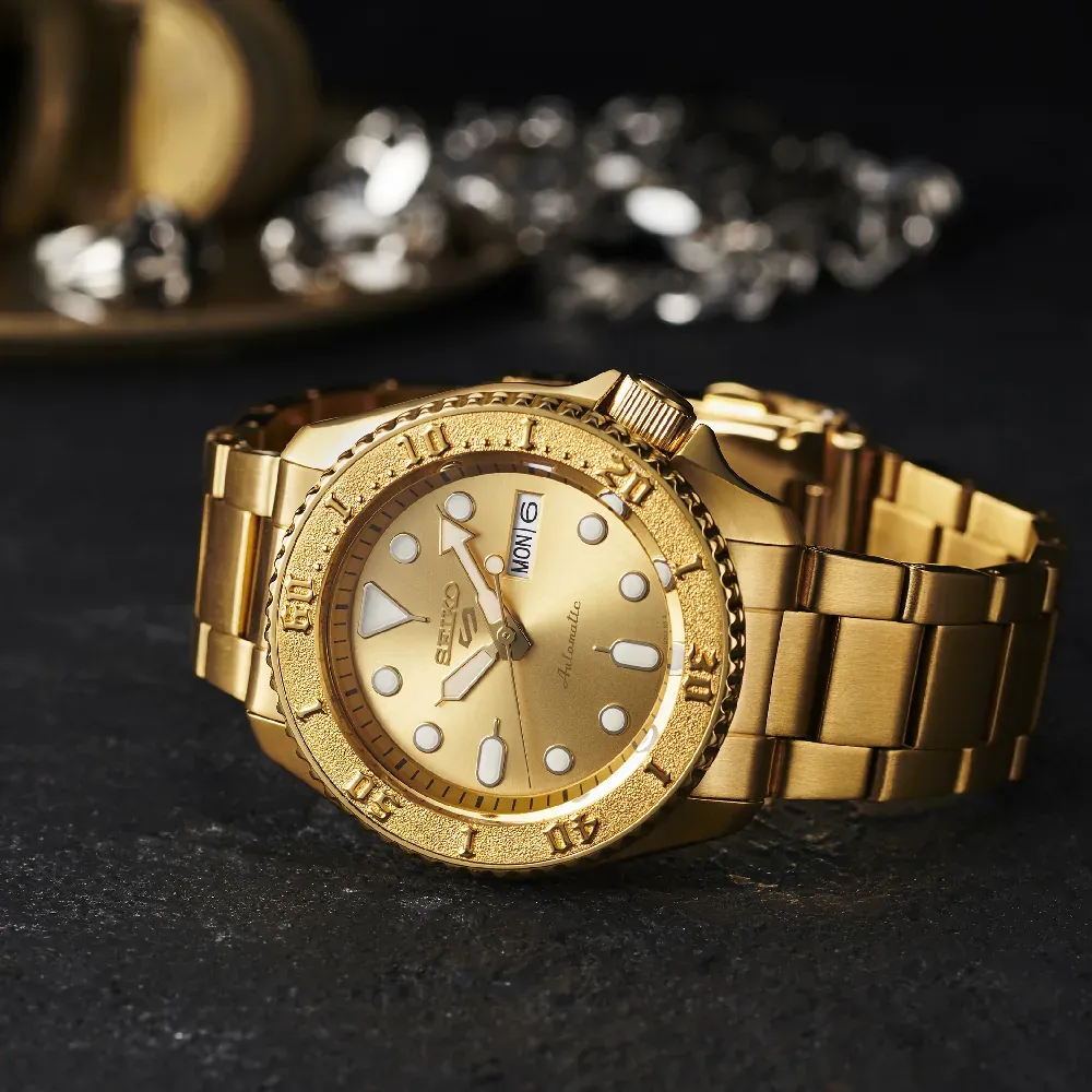 Reloj dorado en plano tres cuartos sobre superficie oscura texturizada, fondo decorativo desenfocado
