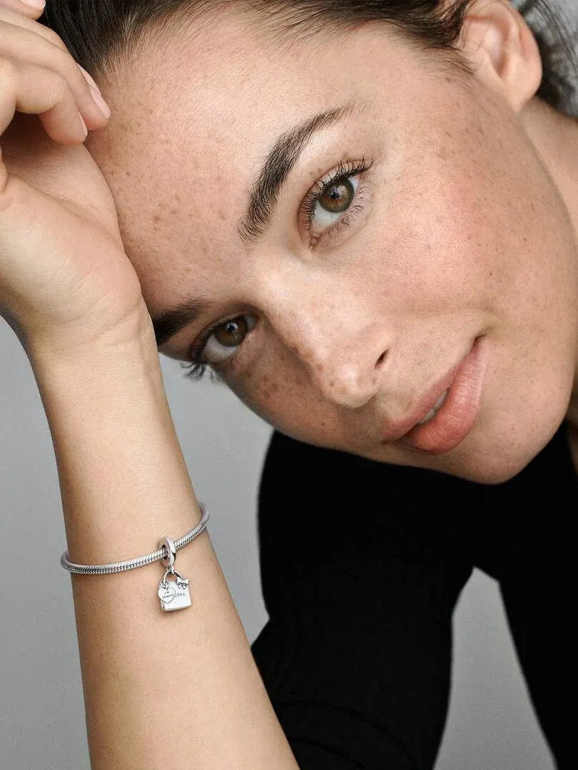 Nahaufnahme des Shoppingtas-Charms am Handgelenk, Model mit unscharfem neutralem Hintergrund.