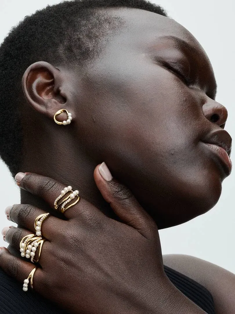 Close-up of hand and profile wearing double band ring and pearl earring, neutral background.